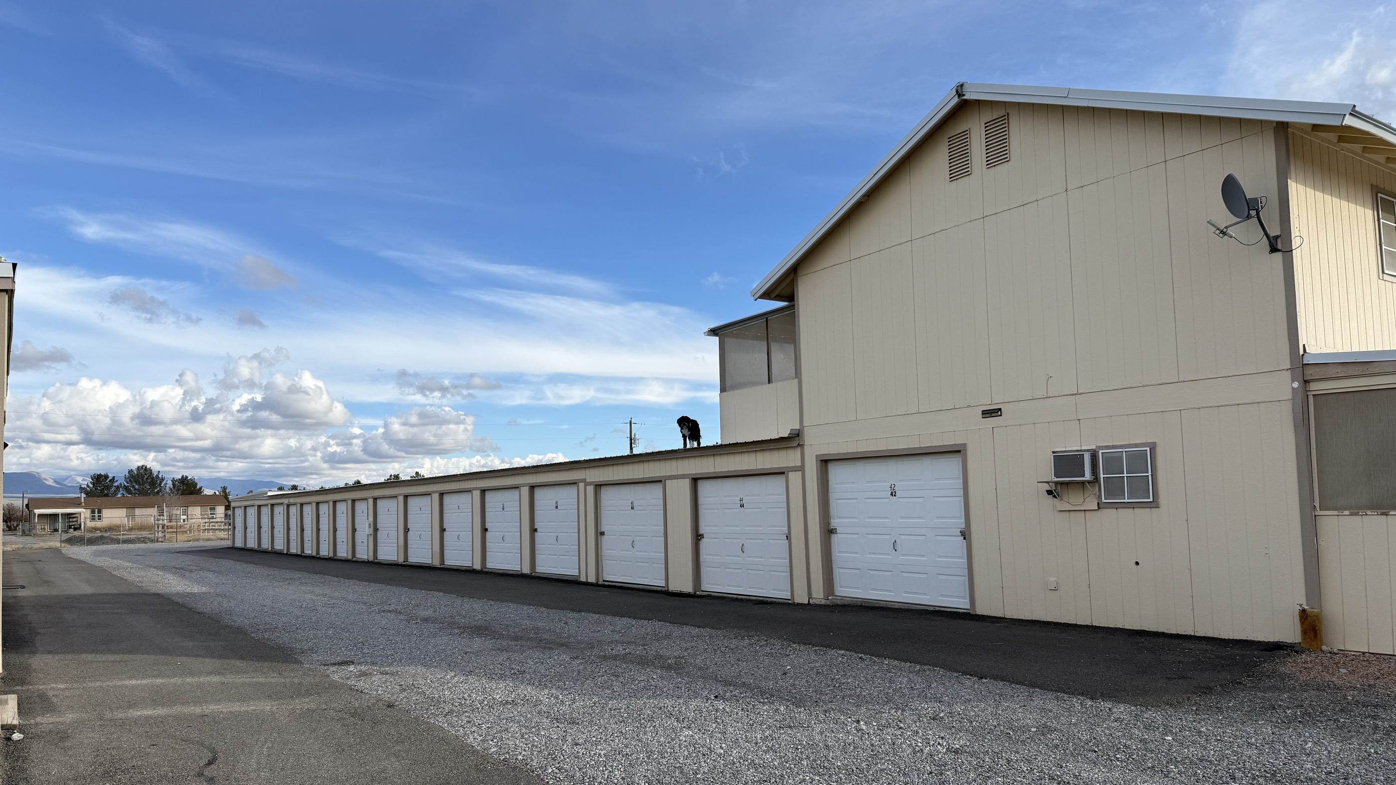 A long row of white roll-up doors at Decroff Storage Units, with the two-story building at the end and the Nevada mountains behind it.